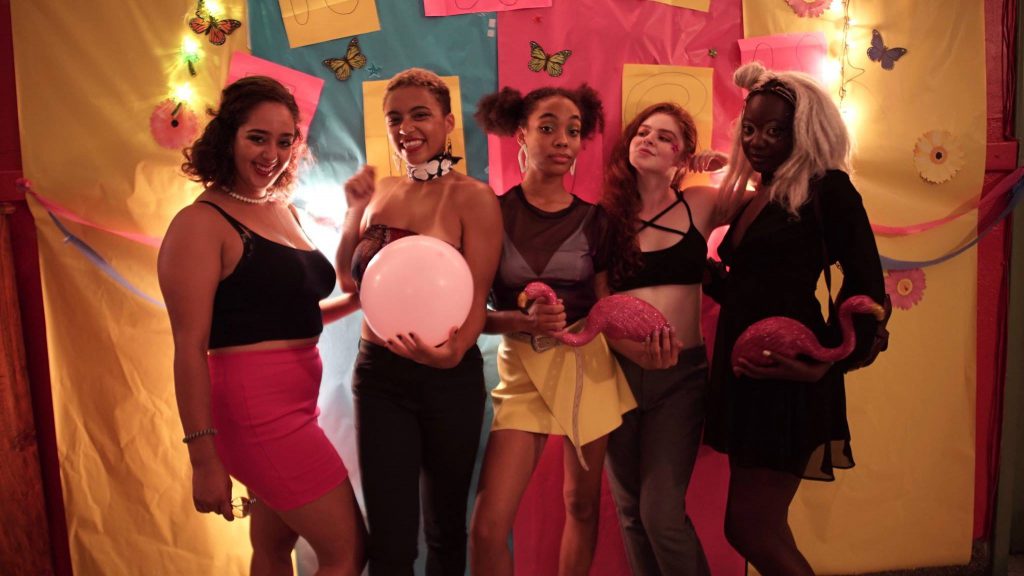 A group of five people dressed in party clothing against a bright backdrop.