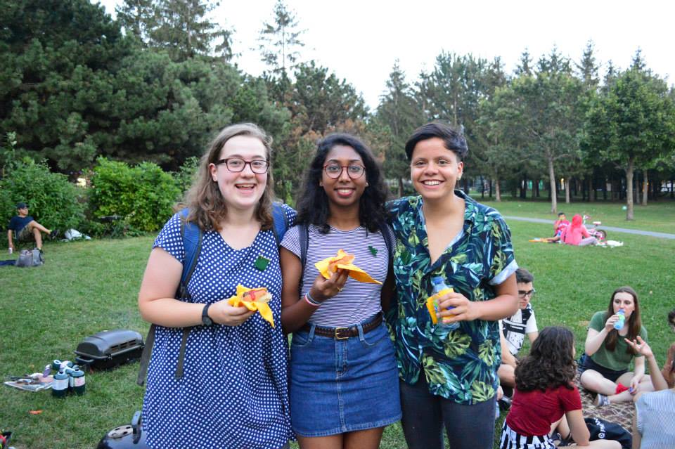 Three people holding hot dogs and smiling in a park.